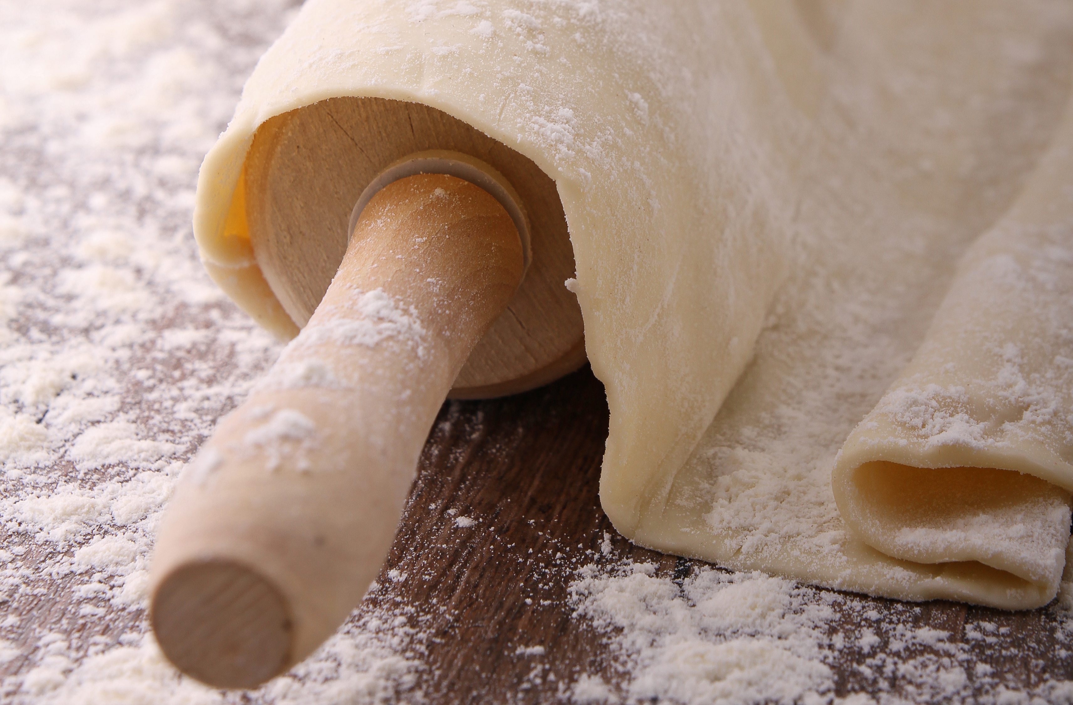Flattened pizza dough draped over a wooden rolling pin