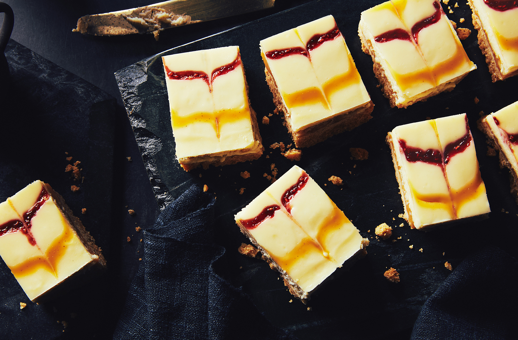 Des carrés de gâteau au fromage au chocolat blond et aux framboises placés sur une ardoise noire pour la présentation
