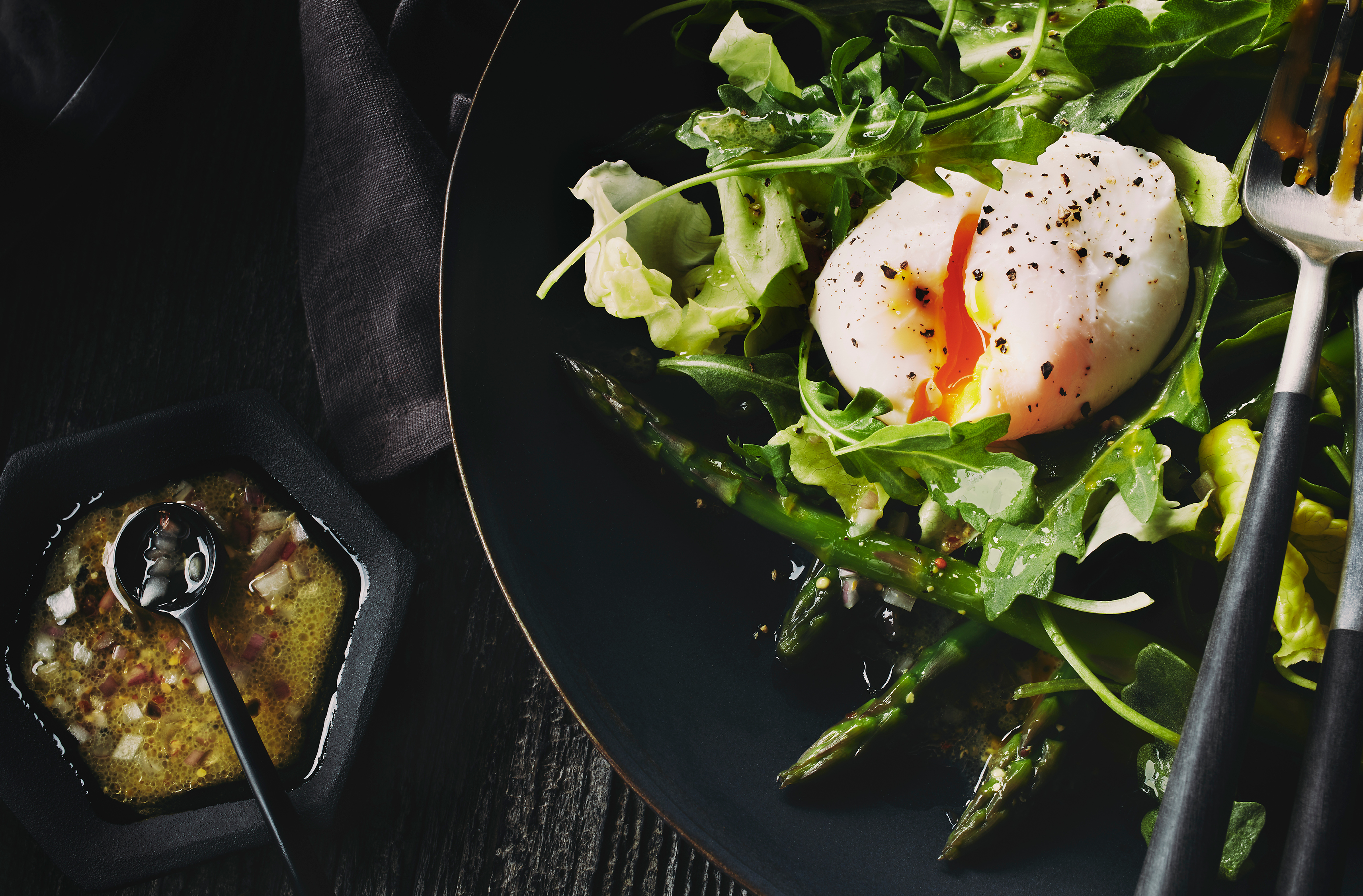 A plate of asparagus and mixed greens topped with umami aioli & a poached egg