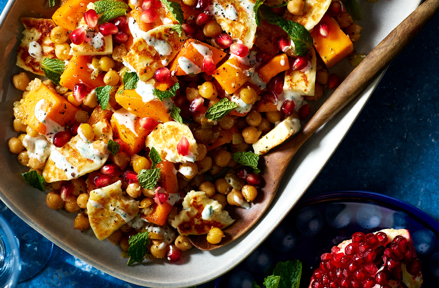 Pomegranate sits beside a dish of diced squash, chickpeas, mint and halloom