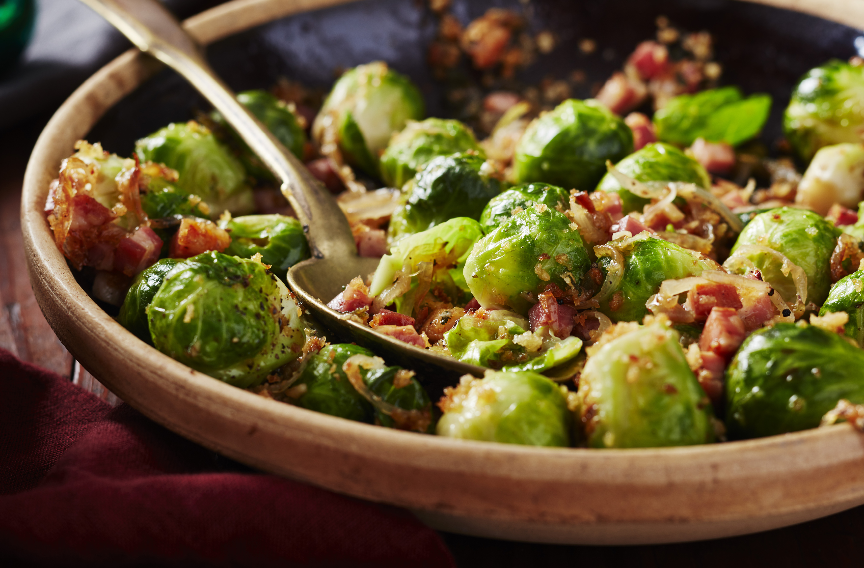 A bowl cradles a spoon and seasoned Brussels sprouts with diced pancetta

