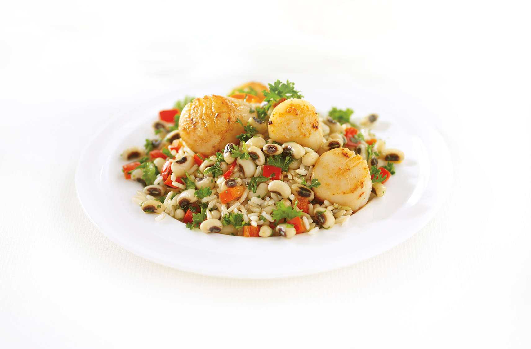 three pieces of pan fried scallops sitting on top of garlicky black-eye peas all placed on a white plate for serving