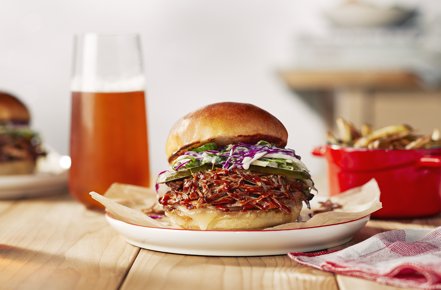 A pulled pork sandwich topped with a creamy slaw on a plate next to a serving of fries and a drink