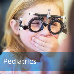 Little girl smiling with phoropter with banner copy overlay "Pediatrics"