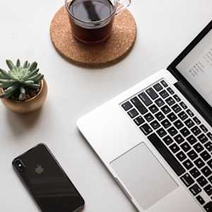 An overhead shot of a laptop, iPhone, cup of tea or coffee, and a small potted succulent