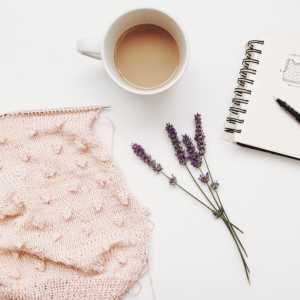 Piece of knitting with cup of coffee, sprig of lavender, and a notebook