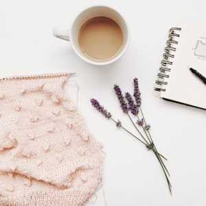 Piece of knitting with cup of coffee, sprig of lavender, and a notebook