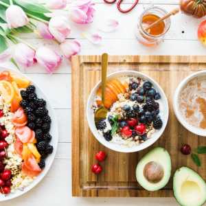 Dishes with healthy fruits, cereal, avocados, a jar of honey, and a bunch of tulips