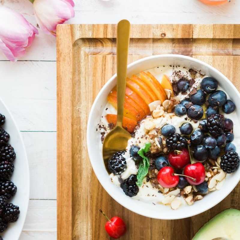 Dishes with healthy fruits, cereal, avocados, a jar of honey, and a bunch of tulips