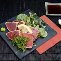 Fancy plate of seared ahi tuna salad on black dish, dark placemat and chopsticks, and bowl of soy sauce