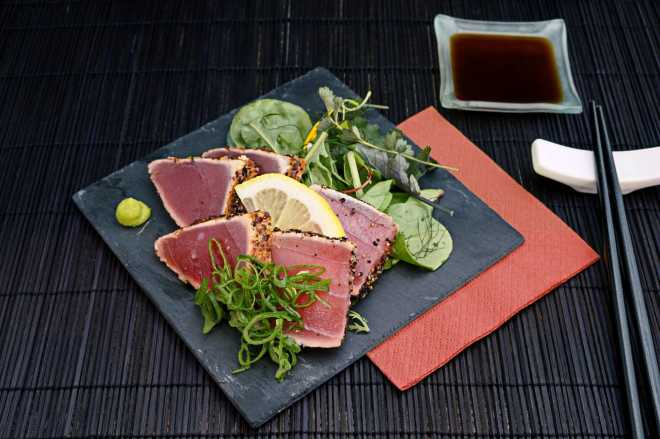 Fancy plate of seared ahi tuna salad on black dish, dark placemat and chopsticks, and bowl of soy sauce