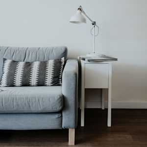 Gray couch with black and white striped pillow and a white end table with lamp