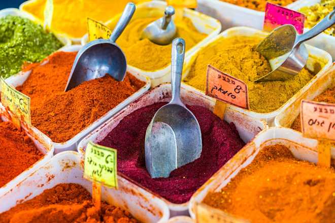 Open bins of colorful red, orange, yellow, and green spices with scoops and price tags