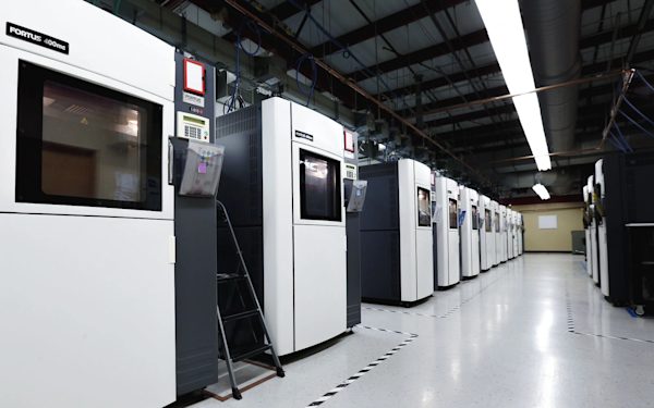 A row of industrial FDM printers in a controlled build room.
