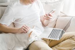 Man sit on a couch with a laptop on his leg and a mobile in his hand.