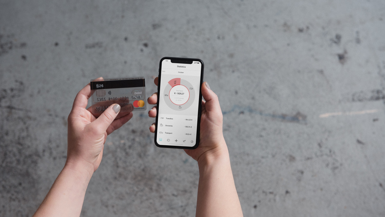 N26 Press Image showing a person sitting while holding the N26 Debitcard Mastercard and her phone