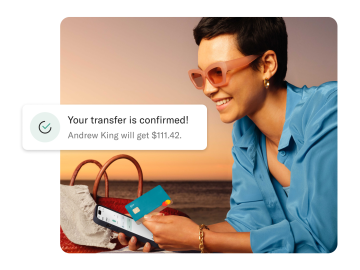Woman on the beach looking at his mobile and holding and N26 You card. In the foreground there is a notification of an cross-border payment.