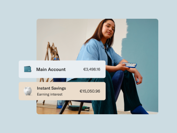 Image showing the balance in the main account and the savings account with a woman dressed in blue holding a cell phone in the background.