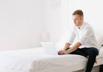 Man working with a laptop on his bed.