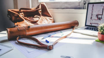 Laptop, Lederrolle und Ledertasche auf einem Schreibtisch.