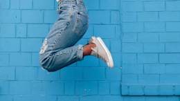 Person in jeans jumping against blue wall.