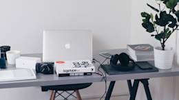 Office desk with camera, laptop, design books and plant.
