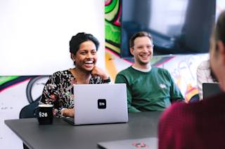 Two people sitting on a meeting room table in front of a computer smiling.