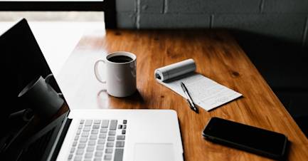 Bureau d'un freelance avec un carnet, un ordinateur et une tasse de café.