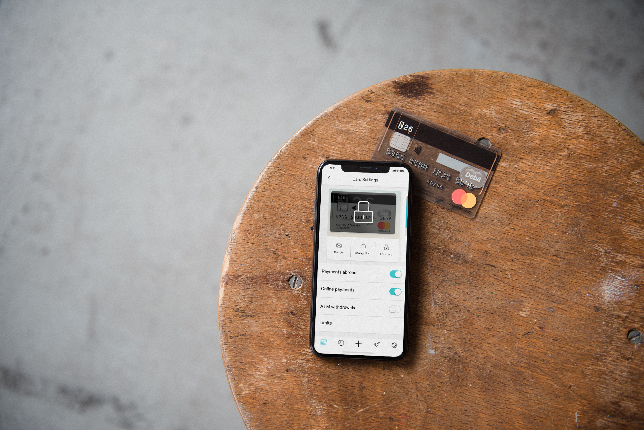 N26 Press Image with a phone showing the card settings section of the N26 app with a bank account card in the background. Both things are laying on a wooden table