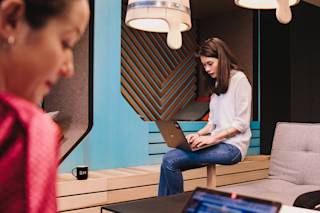 A person sitting on a stool with a laptop on their lap.