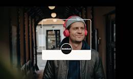A man with red headphones is listening to something and smiling.
