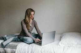 Woman sitting on bed on a laptop.