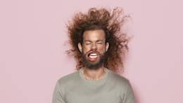 Man with beard and long hair against pink background.