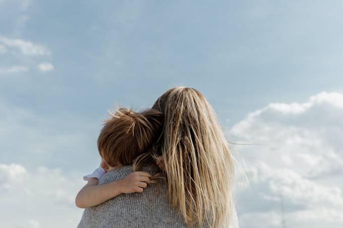 A woman holding a child and looking at the blue sky.
