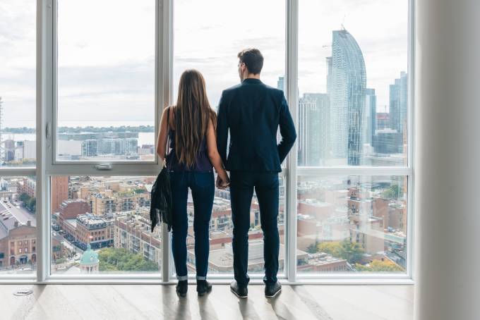 young couple holding hands and looking to the city skyline in an empty apartment.