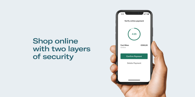 Hand holding smartphone with PSD2 payment confirmation screen displayed.