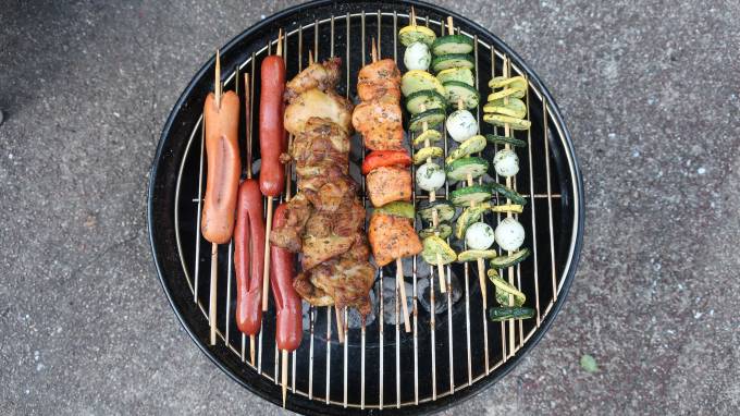 Top view of a BBQ with sausages, beaf, and vegetables.