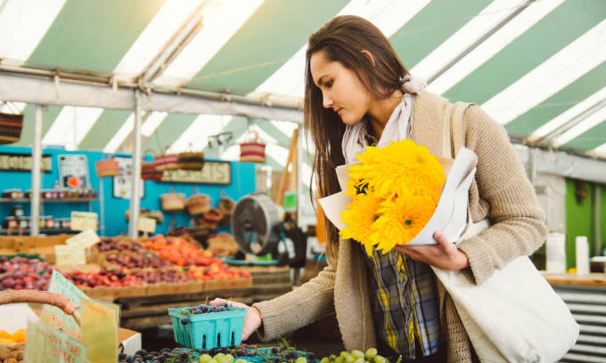 Mujer con ramo de flores comprando en una frutería.