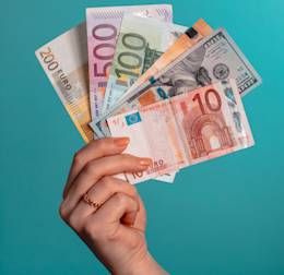 Une main qui tient des billets de différentes monnaies sur fond bleu.