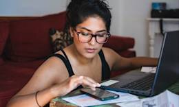 Young woman using phone and laptop to track her debt avalanche strategy.