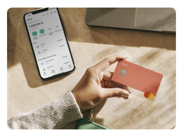 Mano mostrando una tarjeta de N26 Color rubarbo y junto a un mobil con la aplicacion the n26 abierta.