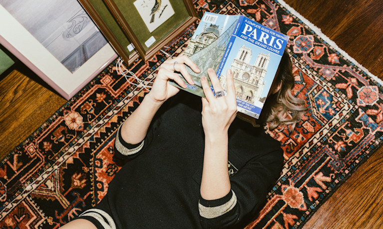 why study abroad, girl reading a book about Paris on a floor