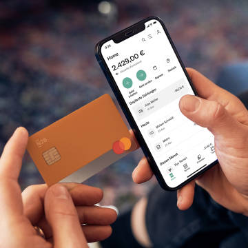 Bild, das eine Person mit einer N26-Debitkarte und der N26-App zeigt, die den Kontofutter mit der Liste der Transaktionen anzeigt.
