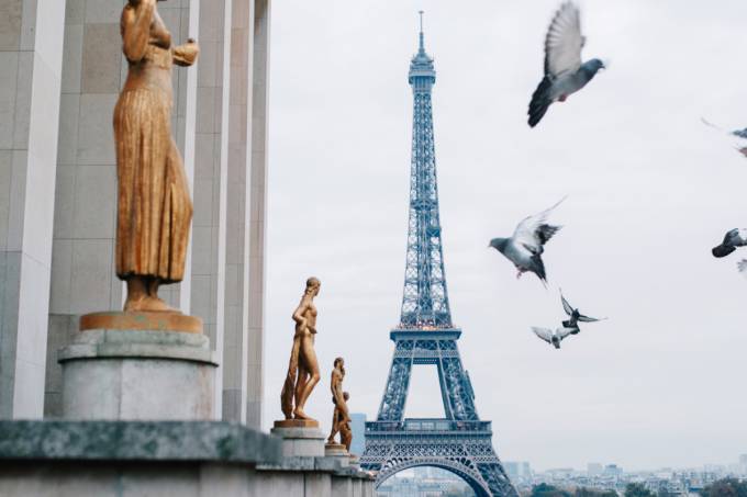 Bild zeigen Tauben in der Nähe einiger Bronzestatuen fliegen und mit dem Eiffelturm im Hintergrund.
