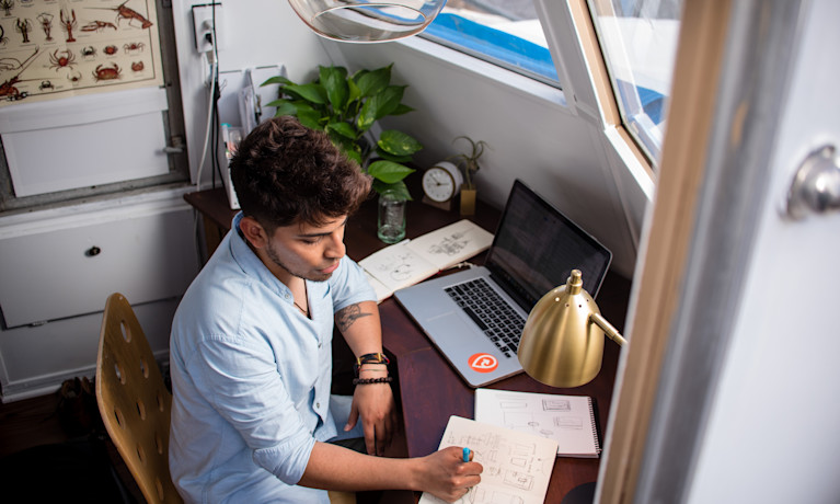 a freelancer writing down his idea on a white book on a small wooden table.