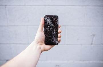 mano que sostiene un smartphone con la pantalla rota.