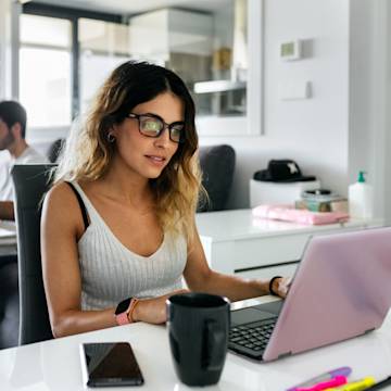 Frau mit Brille arbeitet von zu Hause aus mit einem Laptop.