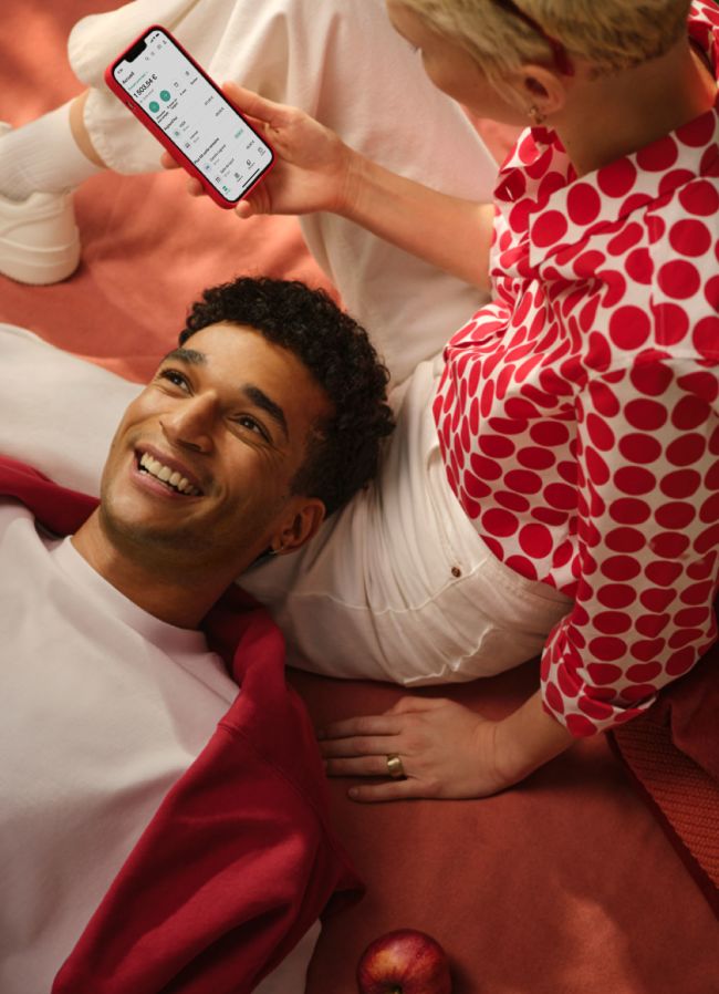 Deux jeunes se détendent sur la couverture en utilisant le smartphone avec l'application N26 dessus tout en souriant.