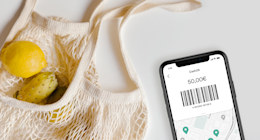 Un sacchetto della spesa con della frutta accanto a uno smartphone con il codice a barre di CASH26.