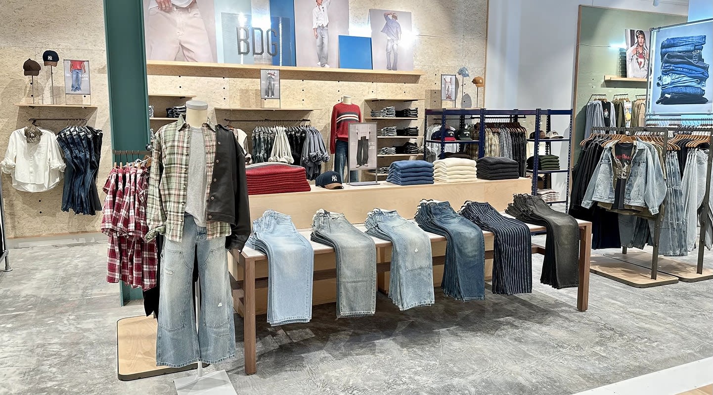 Modern clothing store interior with folded jeans on wooden display table, hanging shirts, and organized shelves with apparel.